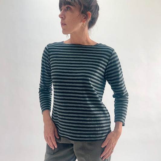 Front view of model wearing an iron stripe 3/4 sleeve boatneck tee in a cotton-linen blend, looking over her shoulder, styled with olive green pants against a white background.
