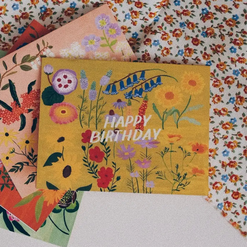 Small Adventure Yellow Floral Birthday Card, colorful illustrated flowers on a mustard yellow background with white “Happy Birthday” lettering.
