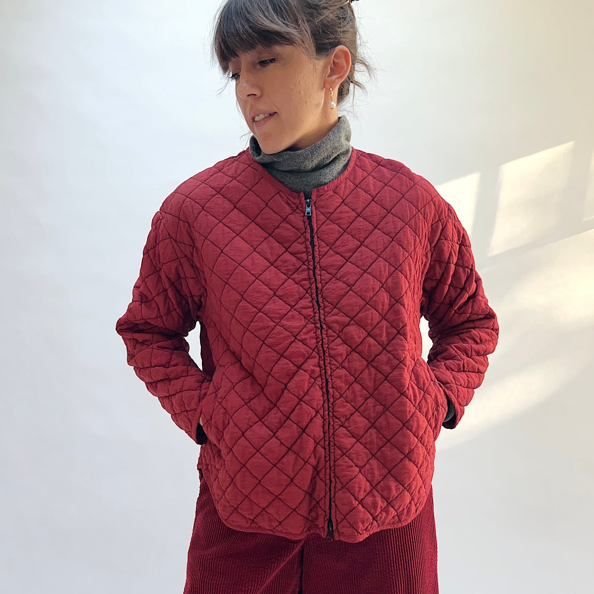 Front view of the Quilted Bomber Jacket in Maraschino, zipped closed, with the model’s hands in the pockets.
