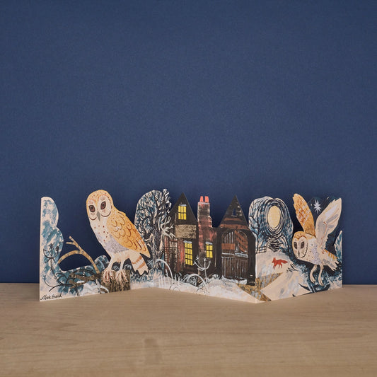 Three Fold Silent Flight concertina card by Mark Hearld, fully extended to show two illustrated barn owls flanking a glowing cottage at night, with a fox in the snow and winter trees, against a navy background