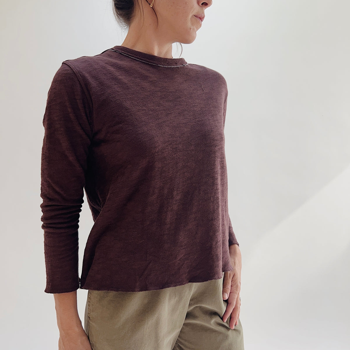 Model wearing the Bryn Walker Double Cotton Tee in Chicory, angled front view showing raw-edge crew neckline, double-layer texture, relaxed silhouette, and slightly cropped long sleeves in deep chicory burgundy, styled with olive pants
