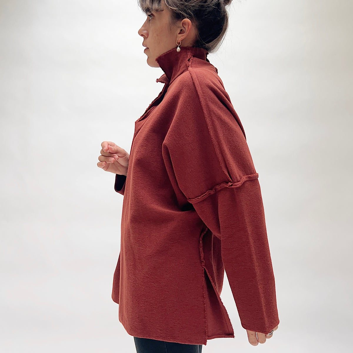 Side profile view of the Eleven Stitch Long Funnel Neck Slub Sweatshirt in Ginger Spice, showing the generous oversized cocoon silhouette, funnel neck, drop shoulders, tunic length, and side slit hem in warm terracotta slub cotton

