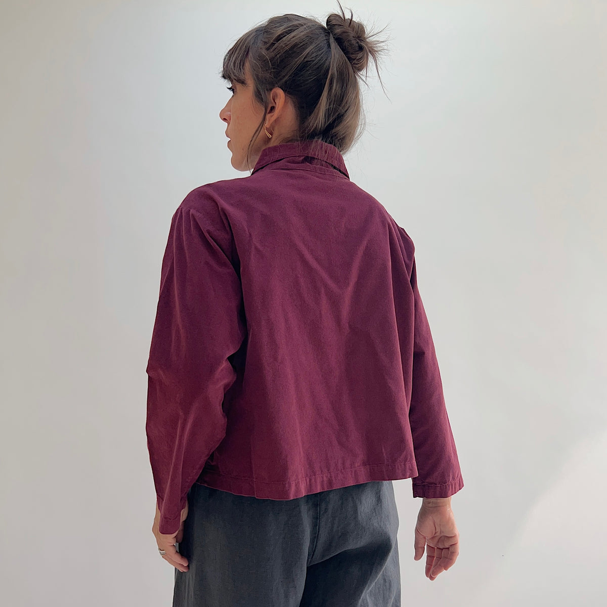 Back view of the Bryn Walker Corduroy Audrey Jacket in Rhone, showing cropped hemline, relaxed silhouette, and burgundy pinwheel corduroy texture, paired with grey trousers
