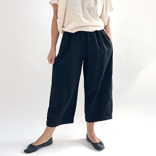 Model wearing the Bryn Walker Heavy Linen Casbah Pant in Black, front view showing fully elastic waistband, two large patch pockets, wide-leg cropped silhouette, and black heavyweight linen, styled with cream top and black ballet flats
