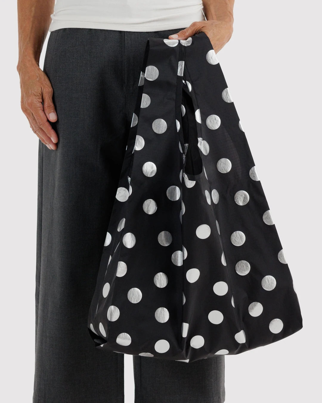 BAGGU Standard Baggu in Silver Metallic Polka Dot, held at a model’s side, showing shiny silver dots on black fabric.
