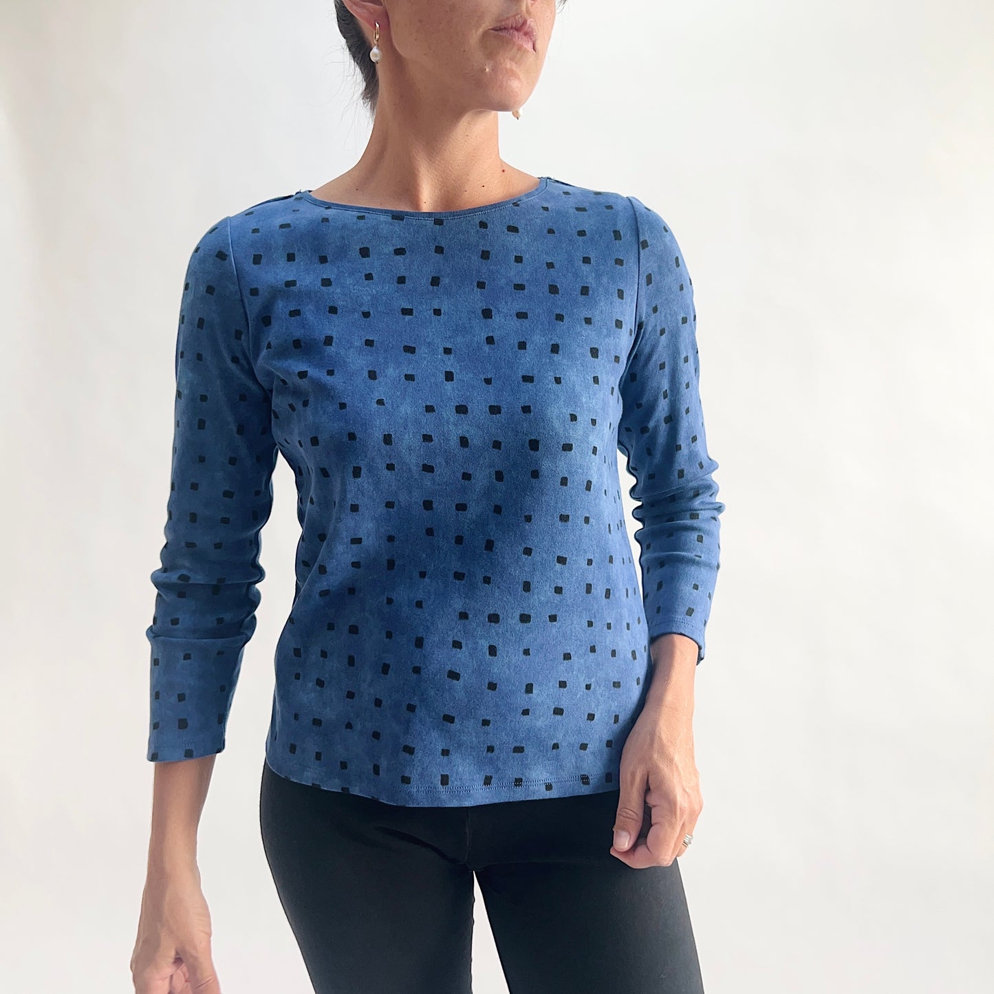 Front view of model wearing a medium indigo long-sleeve cozy rib tee with an all-over tonal dark navy square print, showing the scoop neckline, long sleeves, and relaxed hem, styled with black pants against a white background.
