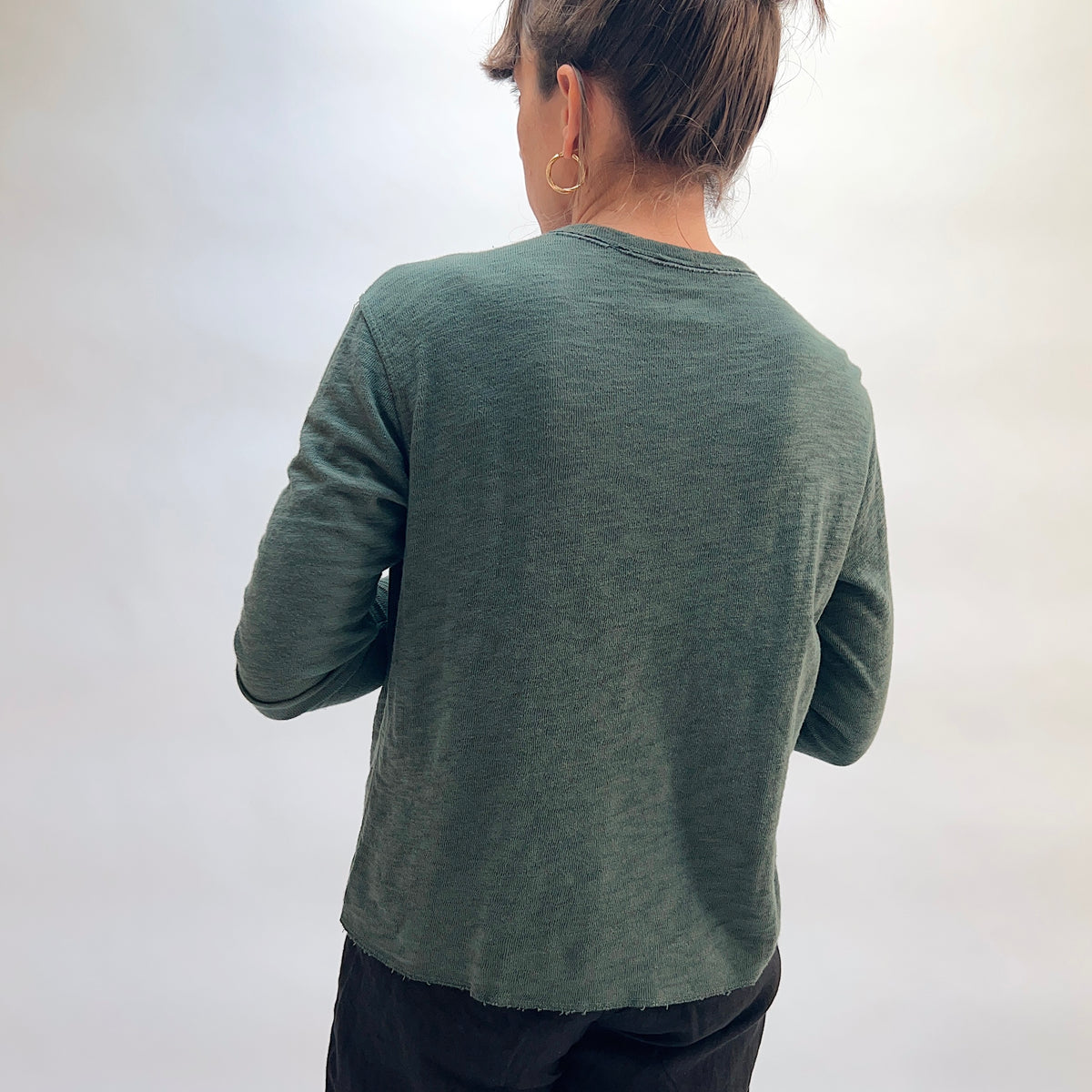 Model wearing the Cut Loose Snap Front Cardigan in Konbu, back view, showing relaxed silhouette and raw curved hem in deep teal green cotton
