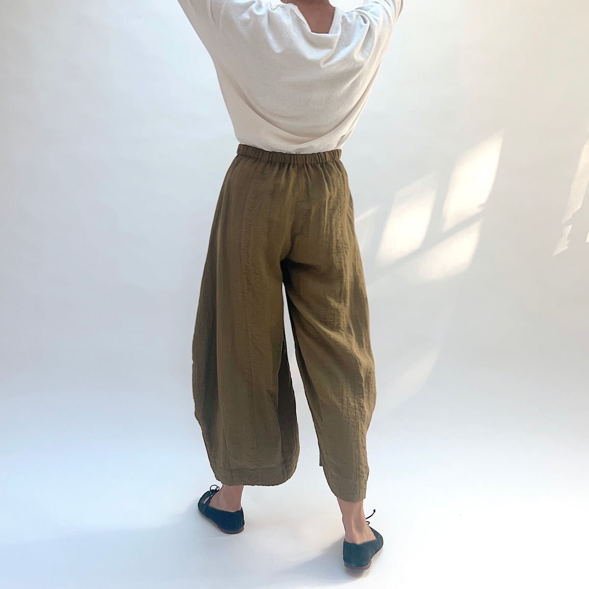 Eleven Stitch Double Pocket Crinkle Travel Pant in Olive, back view showing the gathered waistband and cropped legs.
