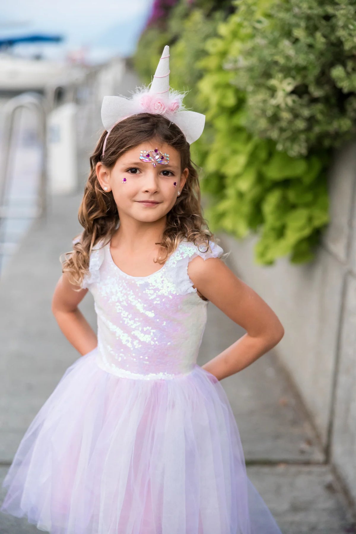 Close-up of a child wearing the Great Pretenders Dreamy Unicorn Dress and Headband, showing the iridescent sequin bodice detail and white unicorn horn headband with pink fluffy ears, outdoors

