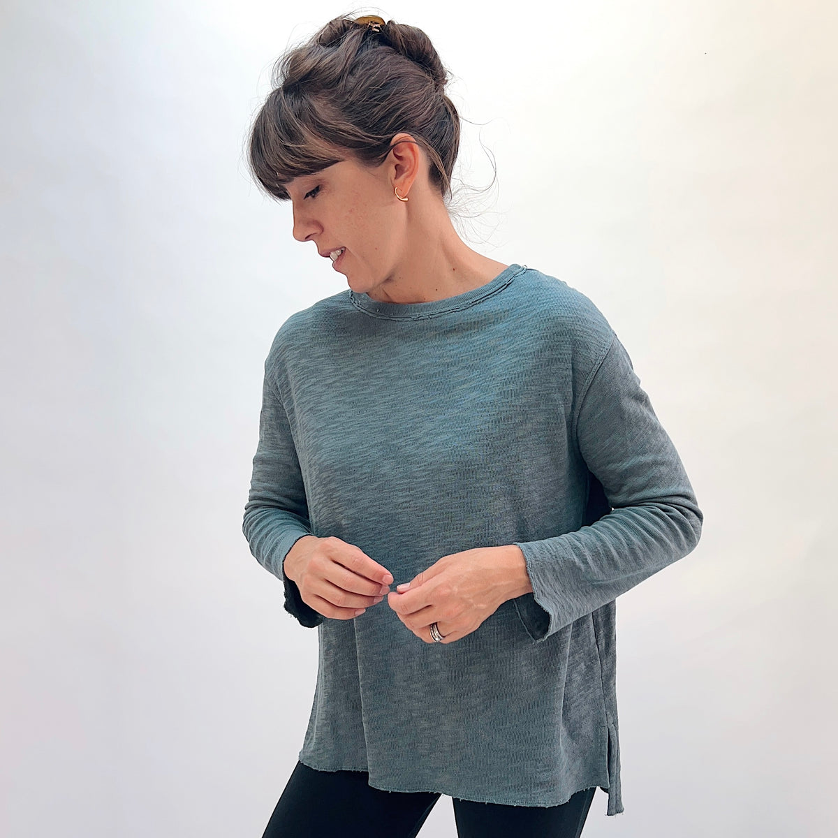 North Star Base Double Cotton Beach Tee in Dusty Denim, front view showing the straight-cut long-sleeve silhouette in dusty teal with exposed raw-edge crew neckline and side slits
