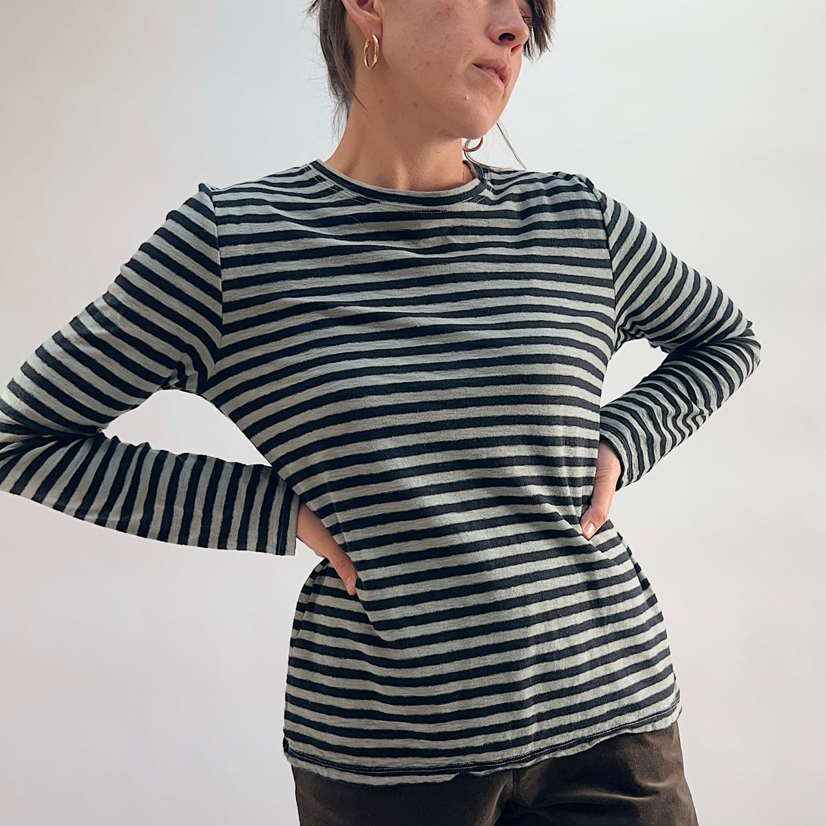 Cut Loose Striped Long Sleeve Easy Tee in Squirrel, black and grey stripe crewneck tee with hands on hips, worn with dark wide-leg trousers — front view showing fit and length
