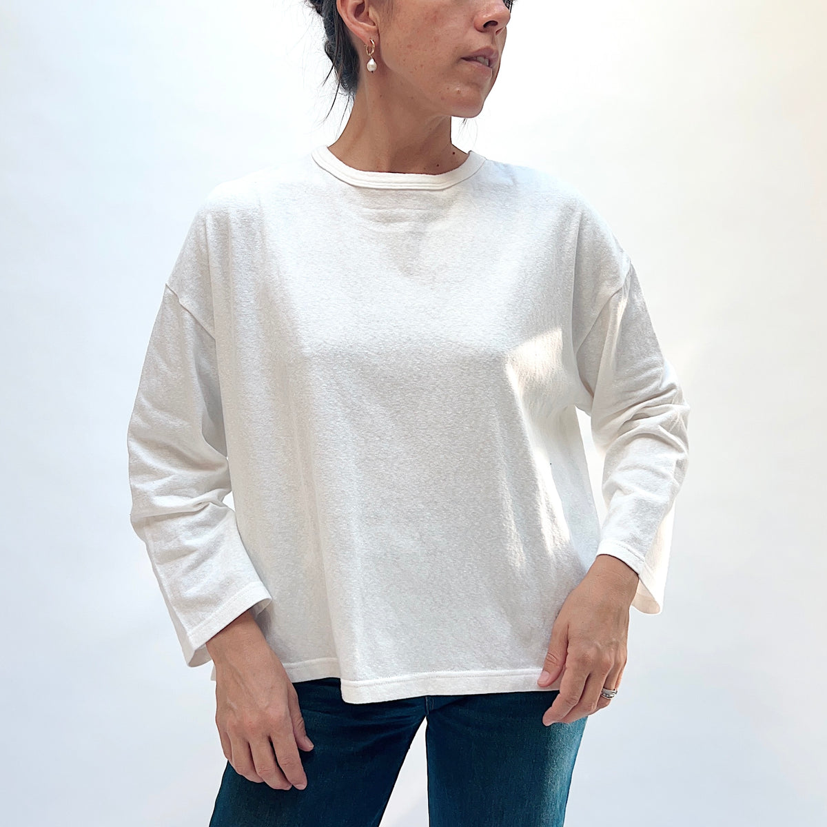 Front view of a model wearing the white cotton knit pullover, showing the round neckline, dropped shoulders, and hem.
