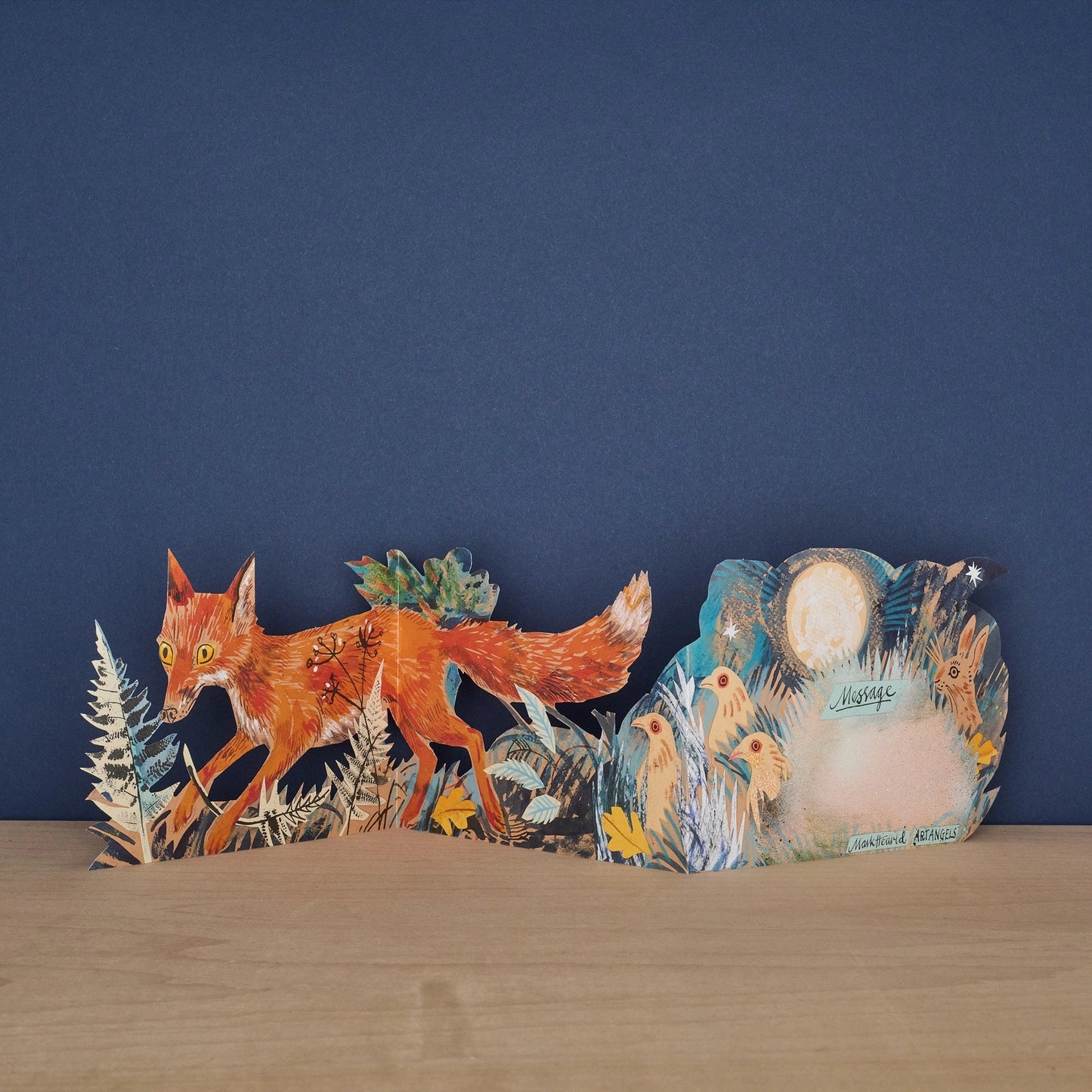 Three Fold Fox concertina card open to reveal blank message panel surrounded by illustrated birds and a hare under moonlight, with fox and fern foliage on the front panel, signed by Mark Hearld and Art Angels