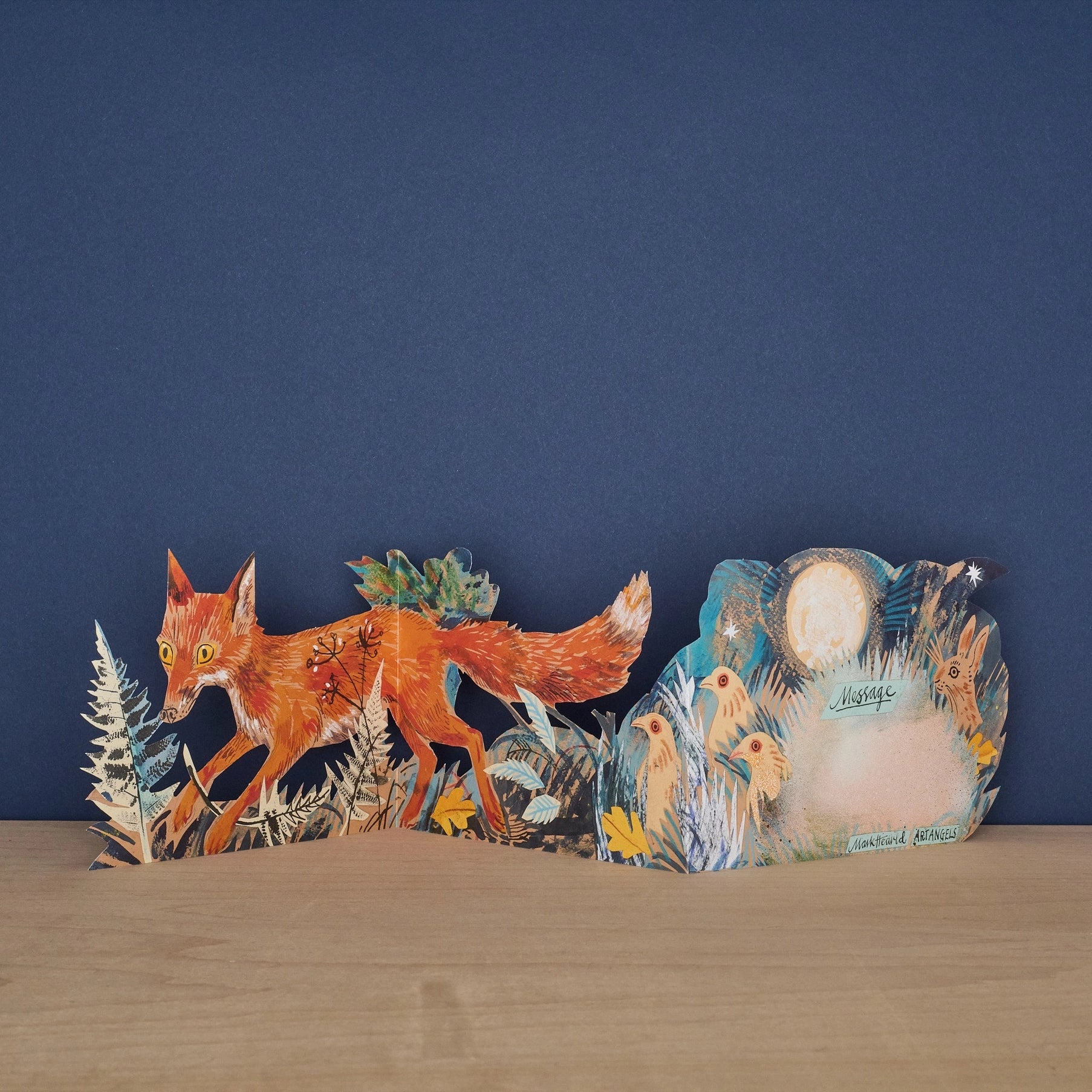 Three Fold Fox concertina card open to reveal blank message panel surrounded by illustrated birds and a hare under moonlight, with fox and fern foliage on the front panel, signed by Mark Hearld and Art Angels