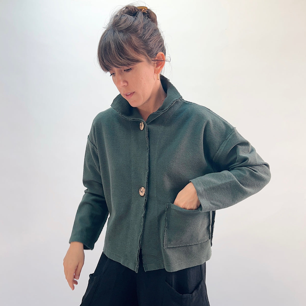 Eleven Stitch Funnel Jacket in Konbu, three-quarter front view showing the hip-length silhouette in forest green cotton terry with high funnel collar, wooden buttons, and large hip patch pocket
