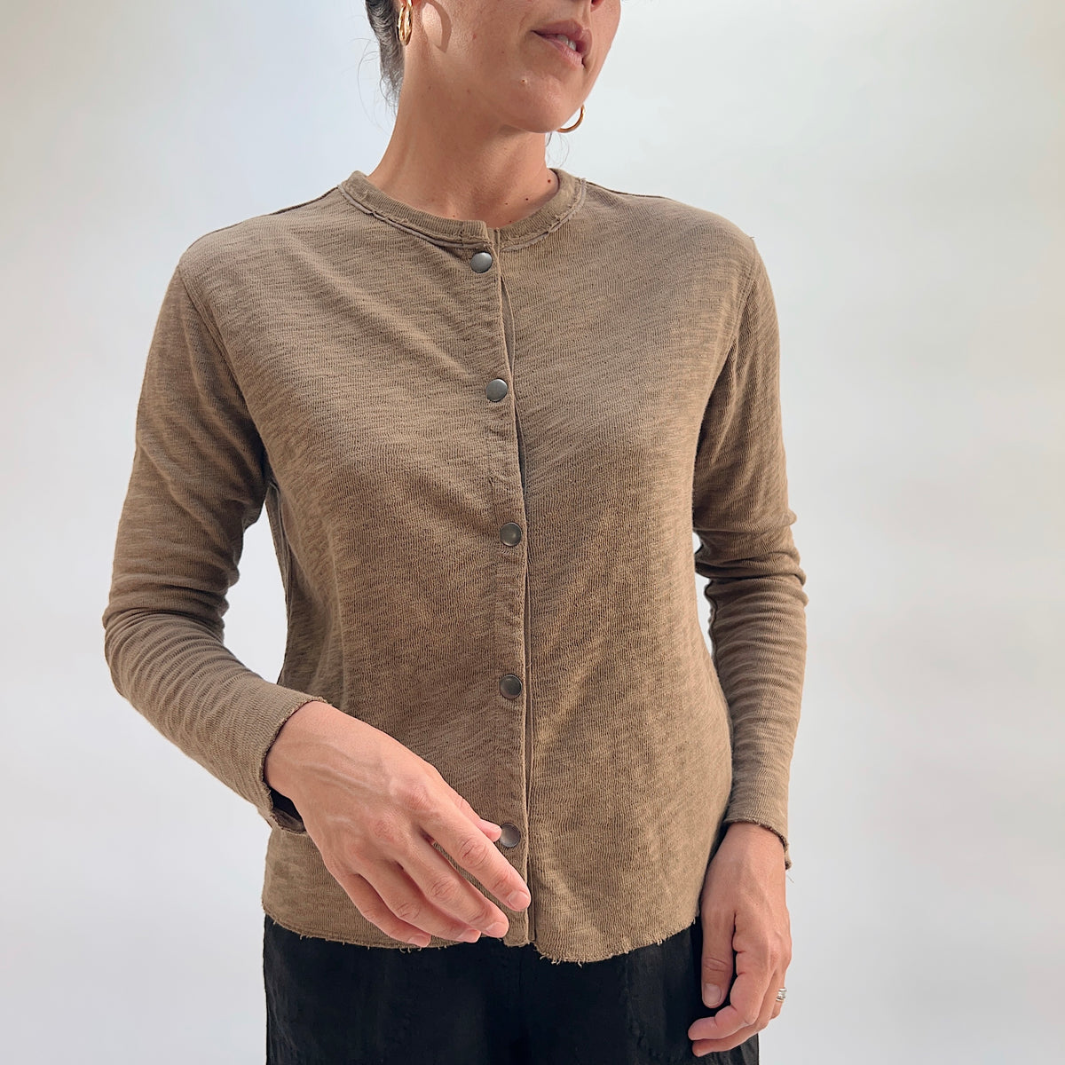 Model wearing the Cut Loose Snap Front Cardigan in Winter Olive, front view, fitted snap-front cotton cardigan in warm olive tan with raw hem, styled with black trousers

