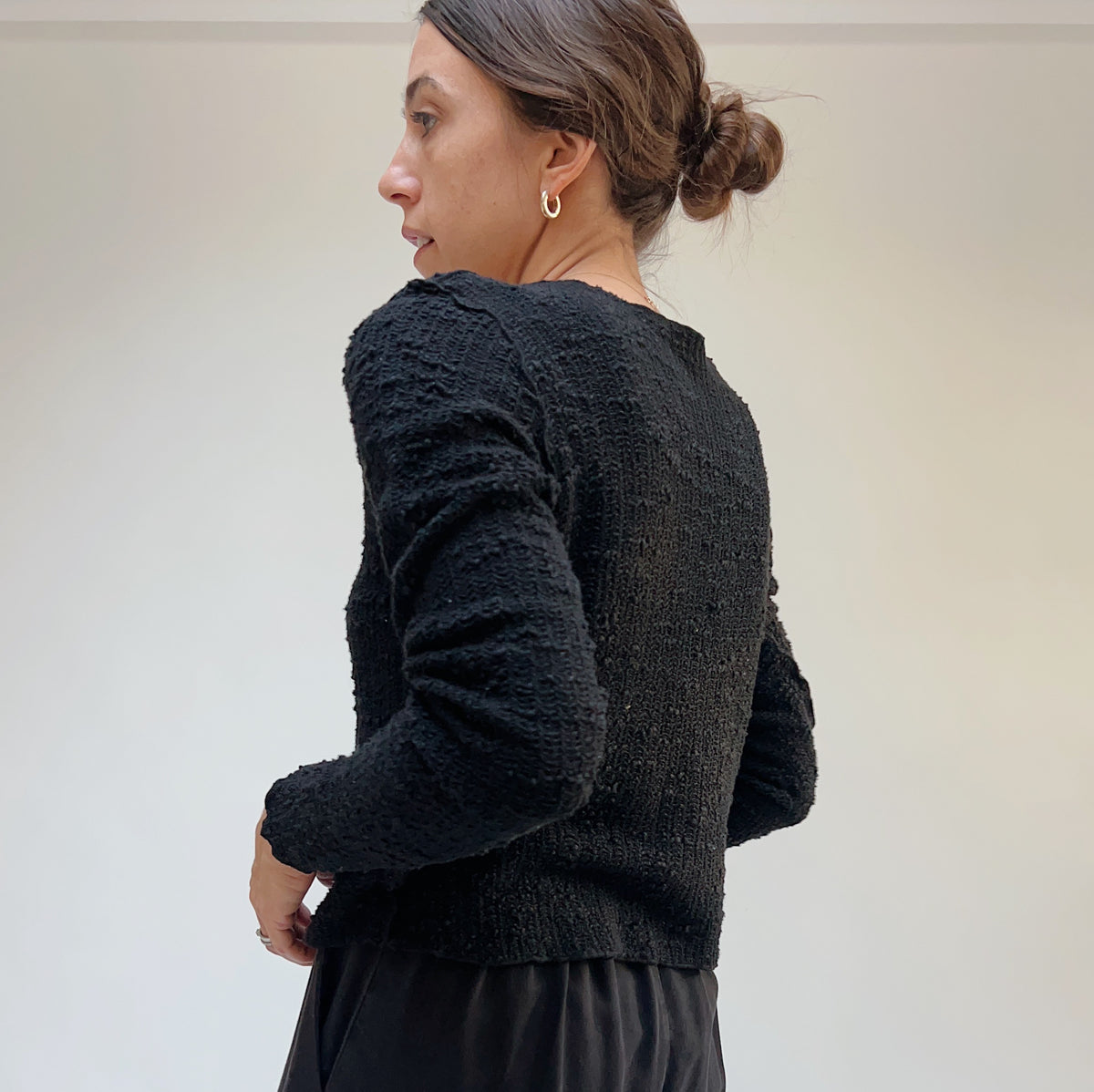 Three-quarter back view on a model of a black textured knit crop cardigan.
