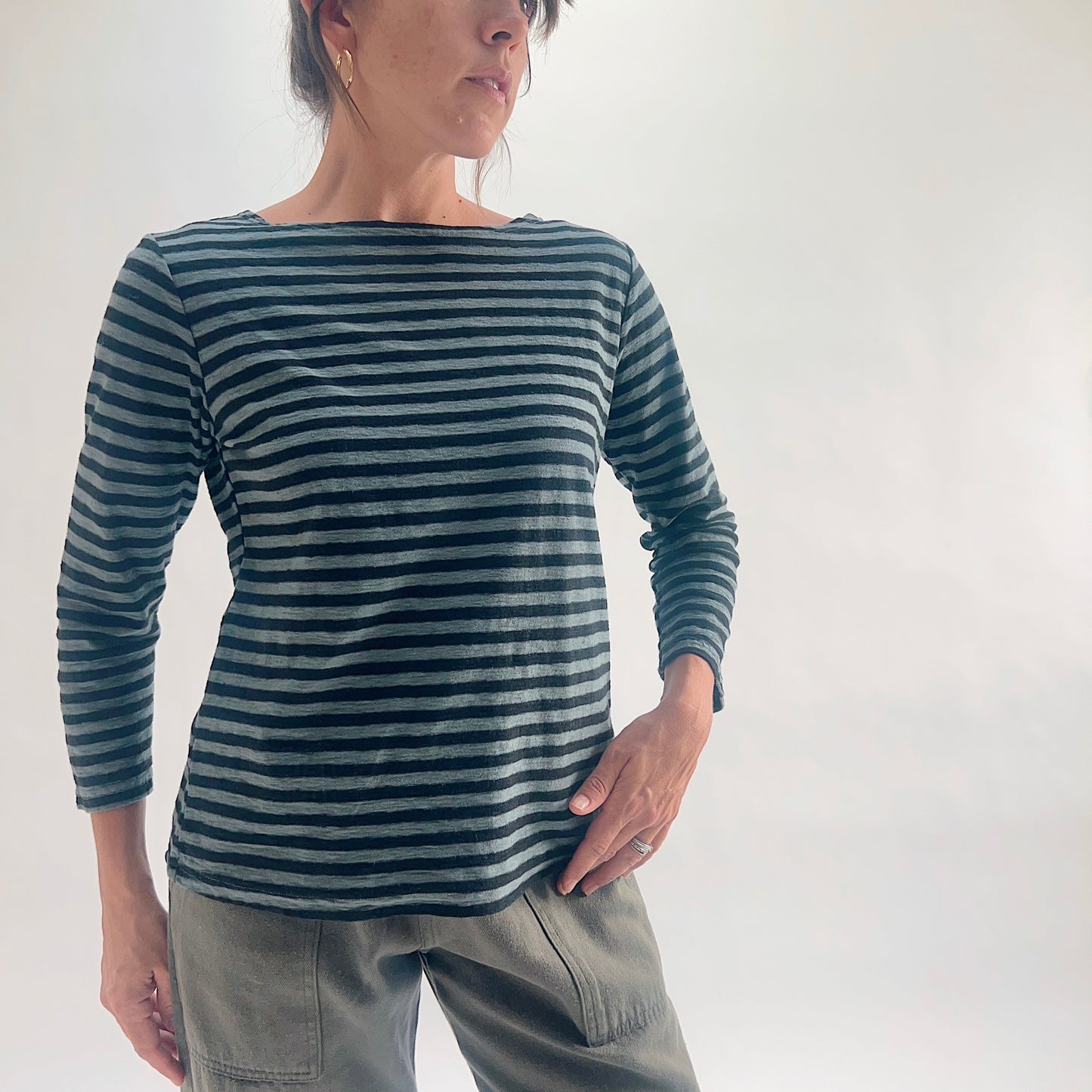Close front view of model wearing an iron stripe 3/4 sleeve boatneck linen blend tee with hand on hip, showing the wide boat neckline and fitted silhouette.
