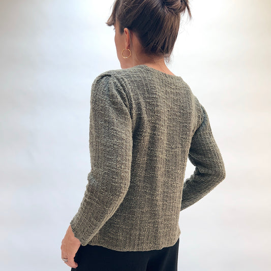 Model wearing the Cut Loose Puff Sleeve Cardigan in Kelp, back view with hair up, showing puffed shoulder seam and textured marled knit of olive green cardigan with long sleeves, styled with black pants

