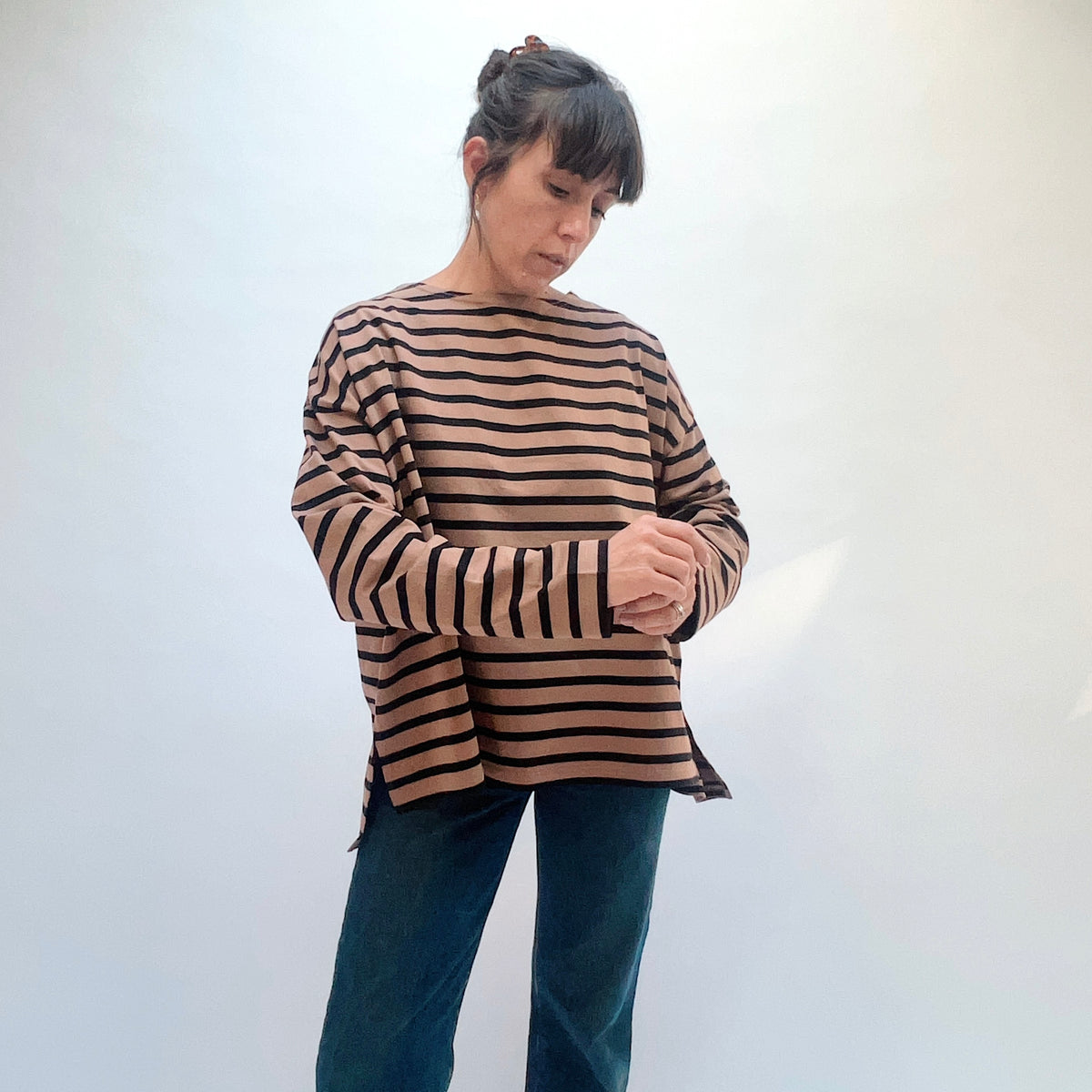Model adjusting a sleeve of the mocha and navy striped knit pullover, worn with blue jeans.
