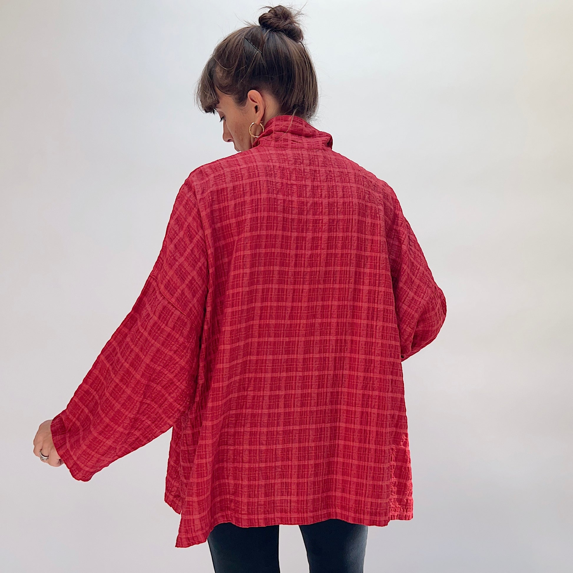 Eleven Stitch Big Shirt in Stripe Crinkle Ruby, back view on model, showing wide crinkle stripe back panel, stand collar, full-length sleeves with cuffs, and curved A-line hem with side slits, paired with black slim trousers
