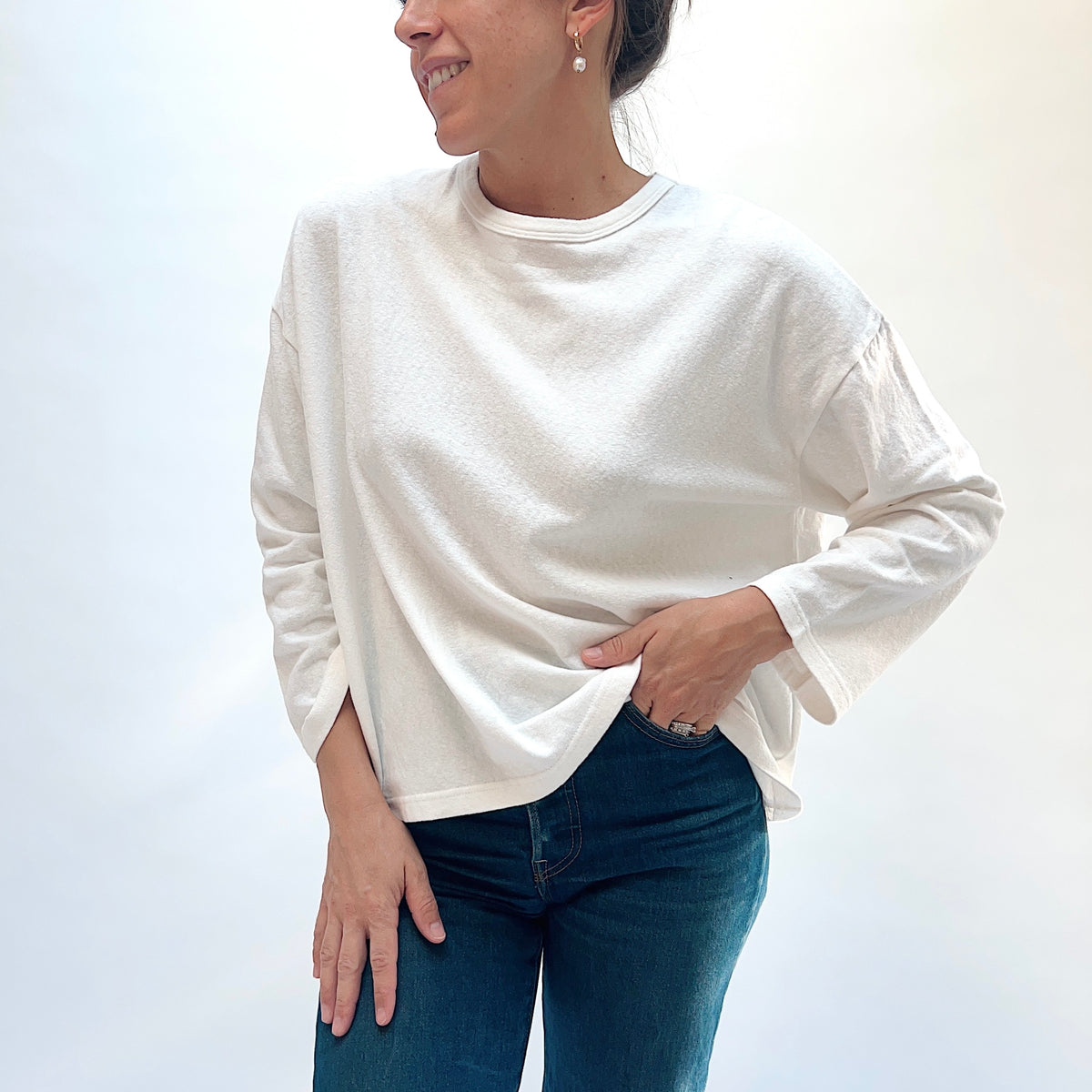 Closer front view of the white cotton knit pullover, showing the round neckline and fabric draping above blue jeans.
