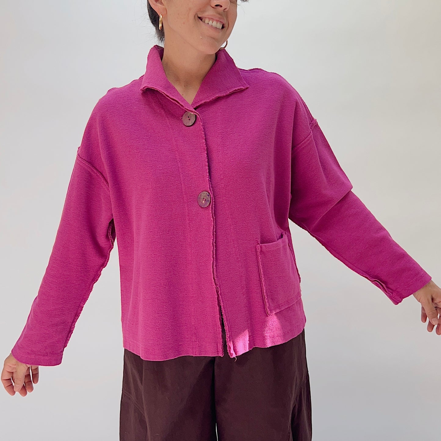 Eleven Stitch Funnel Jacket in Berry, full front view on model, showing funnel collar, two wood button closure, frayed edge detail, and patch pocket, paired with dark brown wide-leg trousers
