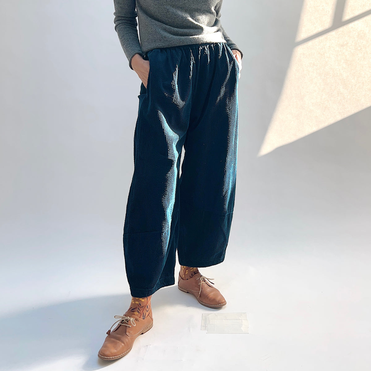 Angled front view of the Lux Corduroy Lantern Pant in Etan, with the model’s hands in the side pockets and the gathered waistband visible.

