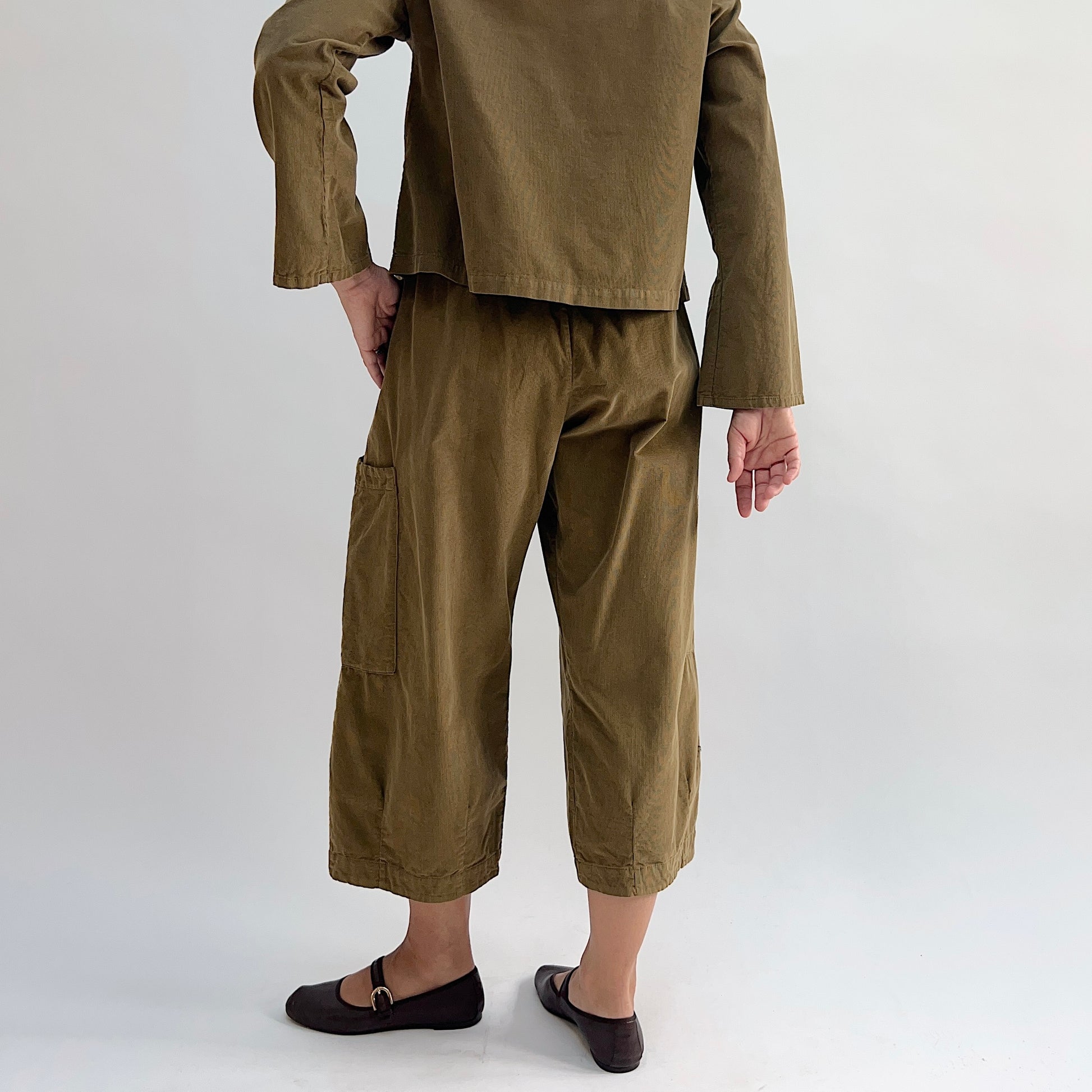 Back view of the Bryn Walker Corduroy Pasha Pants in Partridge, showing elastic waistband, side leg patch pocket, cropped hemline, and relaxed wide-leg silhouette in olive pinwheel corduroy, paired with matching jacket and dark Mary Jane flats
