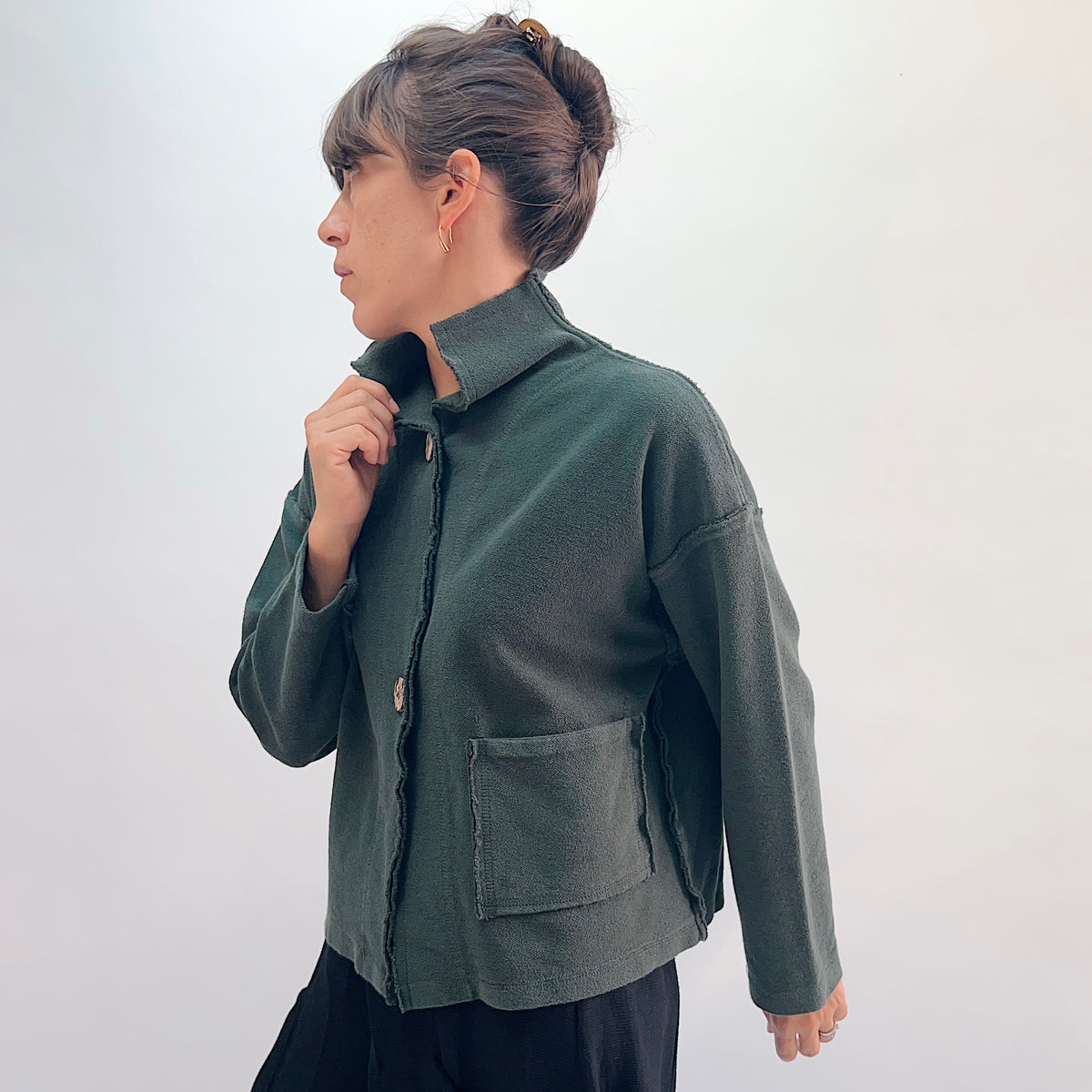 Eleven Stitch Funnel Jacket in Konbu, side view showing the raw-edge seam detail, high funnel collar, and large hip patch pocket in forest green cotton terry
