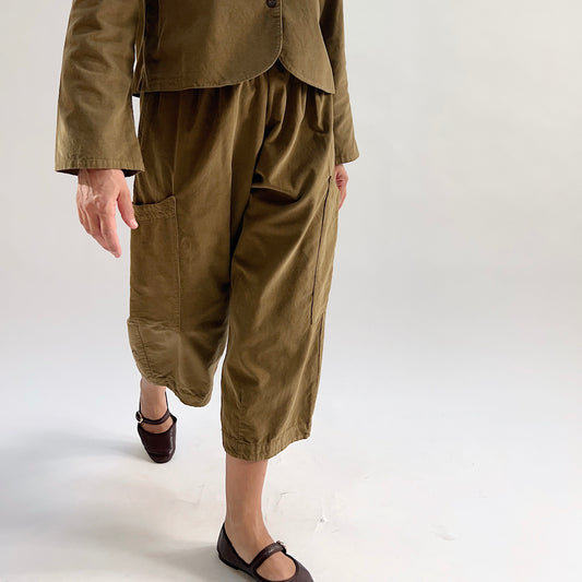 Model in motion wearing the Bryn Walker Corduroy Pasha Pants in Partridge, side view highlighting side leg pocket, cropped wide-leg hem, and olive pinwheel corduroy texture, paired with matching jacket and dark flats
