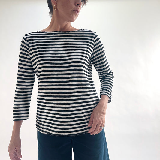 Front view of model wearing a navy and white laundered stripe 3/4 sleeve boatneck tee with a relaxed fit and curved hem, styled with dark blue wide-leg pants against a white background.
