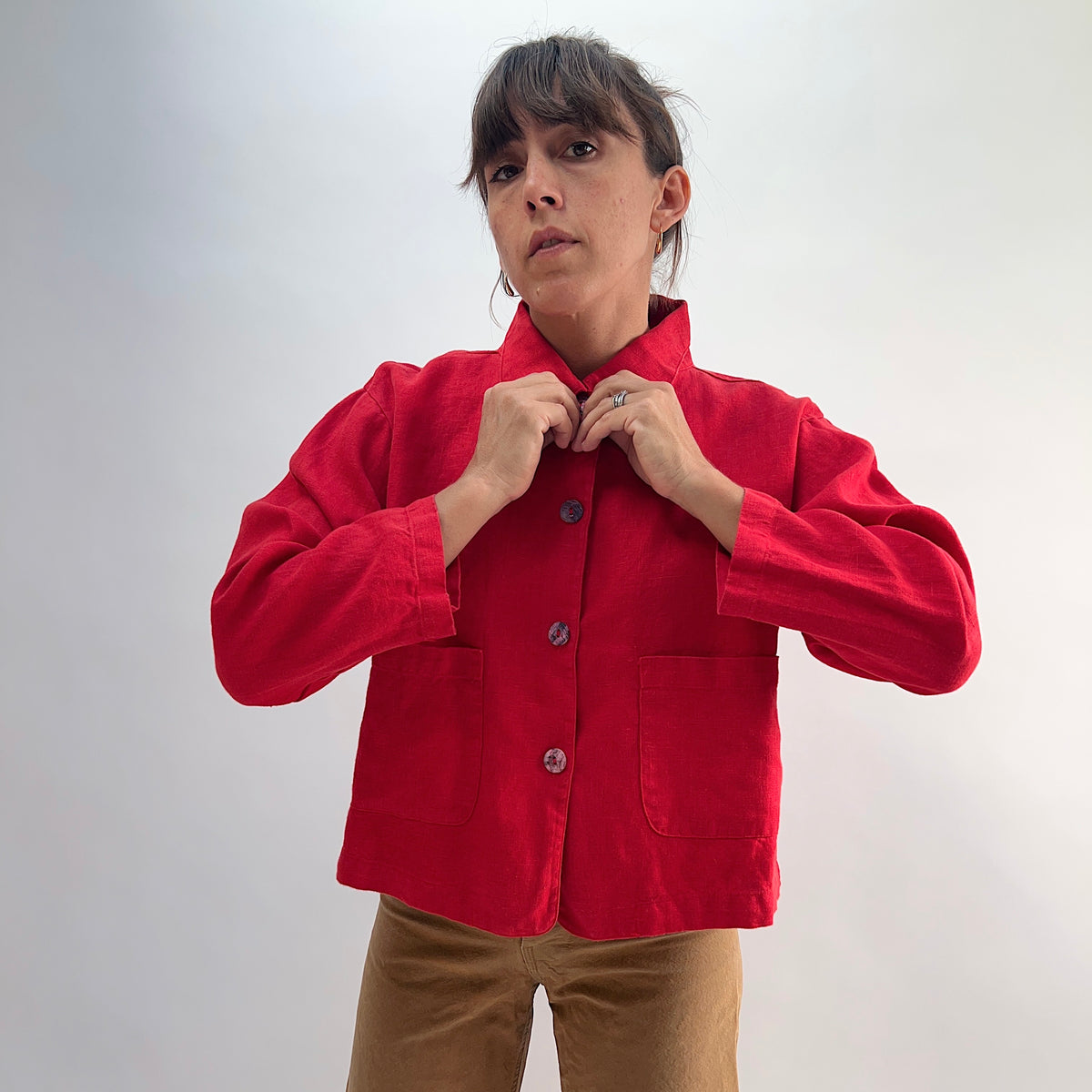 Model adjusting the collar of the Bryn Walker Heavy Linen Audrey Jacket in Hawthorn, showcasing rounded collar and shell buttons, front view
