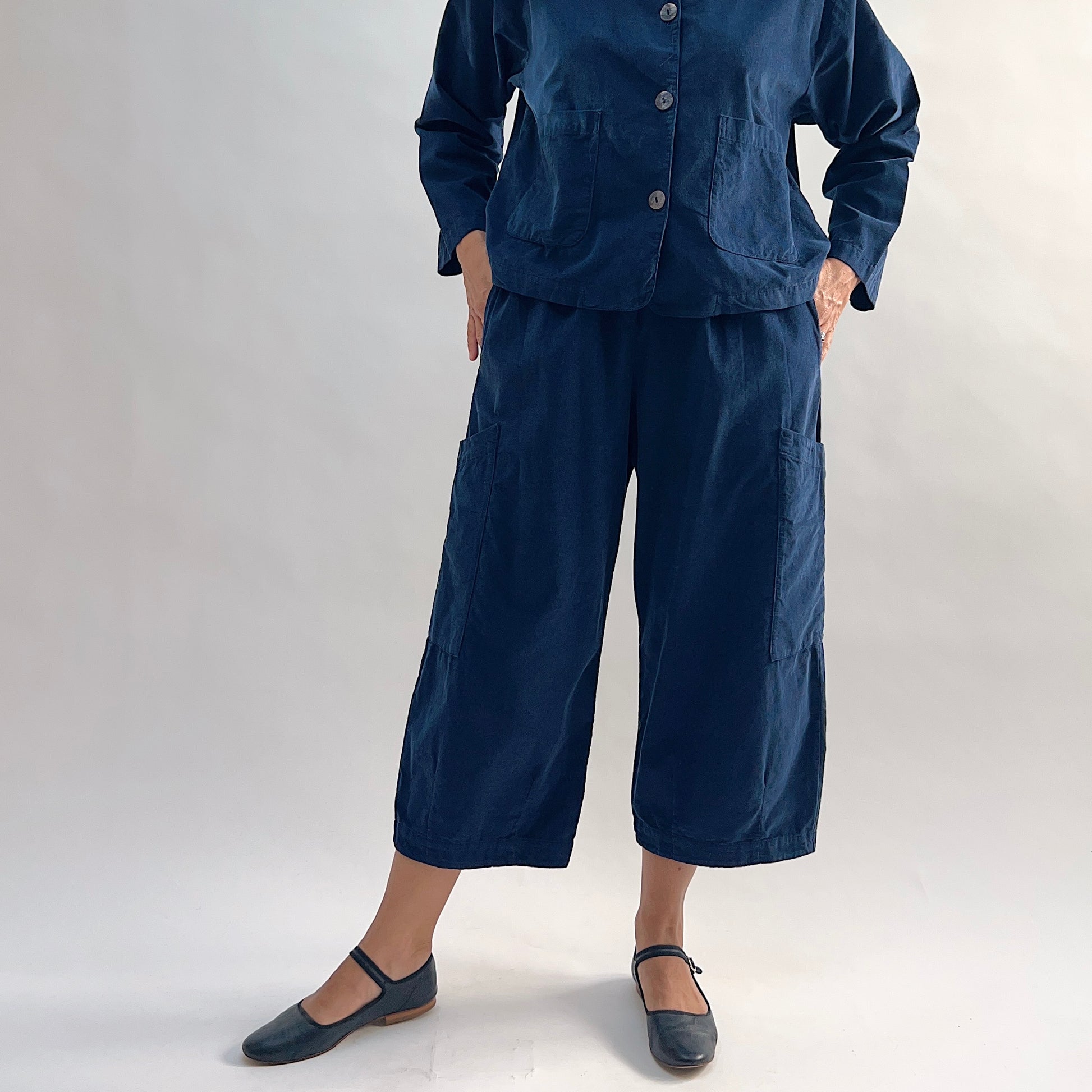 Model with hands in hip pockets of the Bryn Walker Corduroy Pasha Pants in Nova, front view showing relaxed wide-leg silhouette, side leg pockets, and navy pinwheel corduroy texture, with black Mary Jane flats
