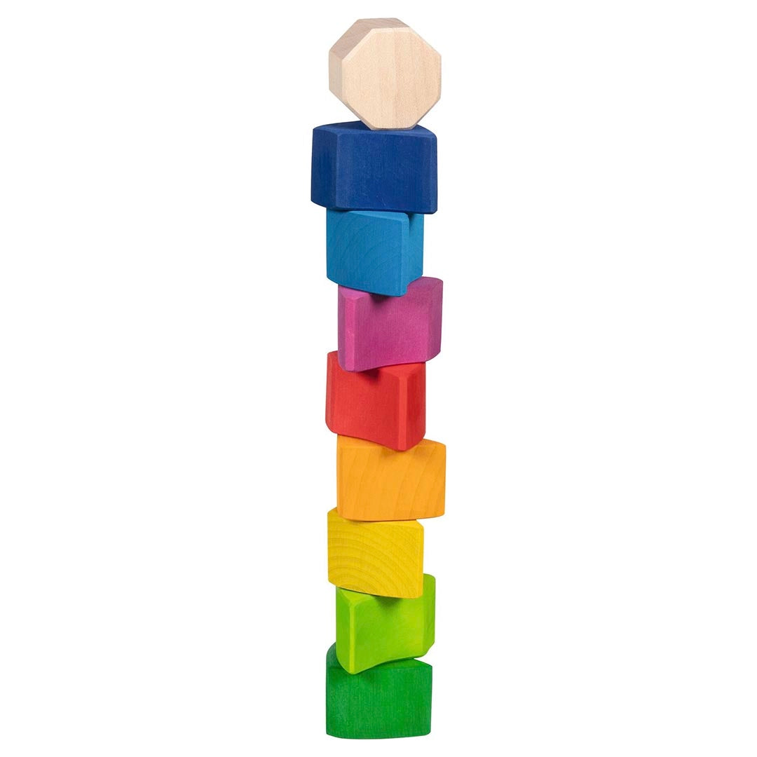 Goki Sassy Snail building blocks stacked in a tall tower on a white background, with the natural wood octagon piece at the top and all 9 colored wedge blocks balanced in a twisting column from dark blue through light blue, pink, red, orange, yellow, lime, and green at the base