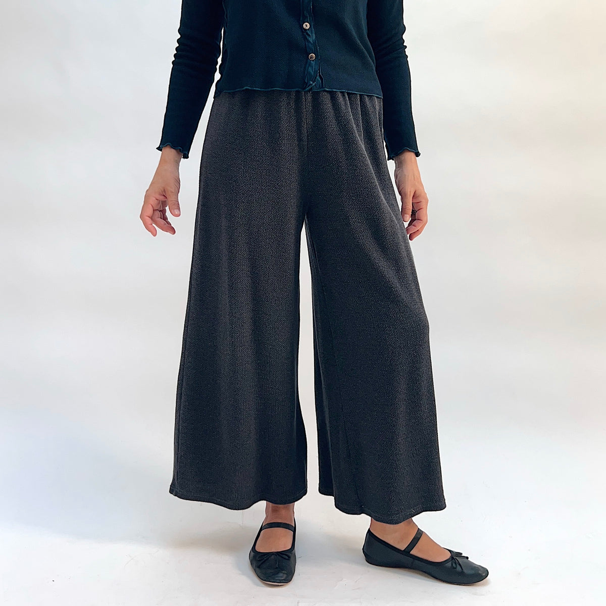 Model wearing the Cut Loose Marled Knit Crop Pant in Iron, front view, showing wide-leg crop silhouette, elastic waistband, and dark charcoal marled knit texture, styled with a dark teal cardigan and black mary jane flats
