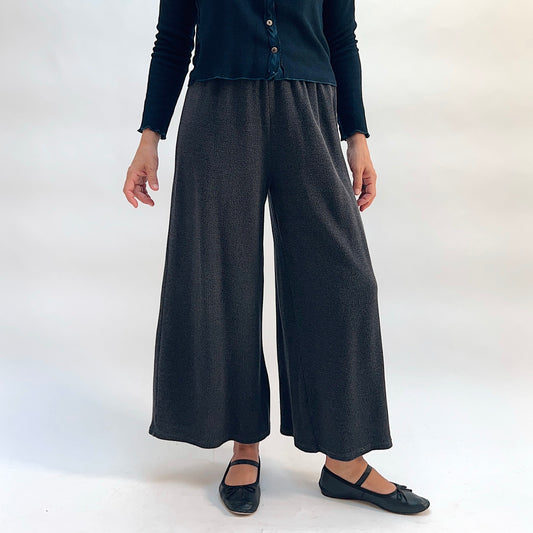 Model wearing the Cut Loose Marled Knit Crop Pant in Iron, front view, showing wide-leg crop silhouette, elastic waistband, and dark charcoal marled knit texture, styled with a dark teal cardigan and black mary jane flats
