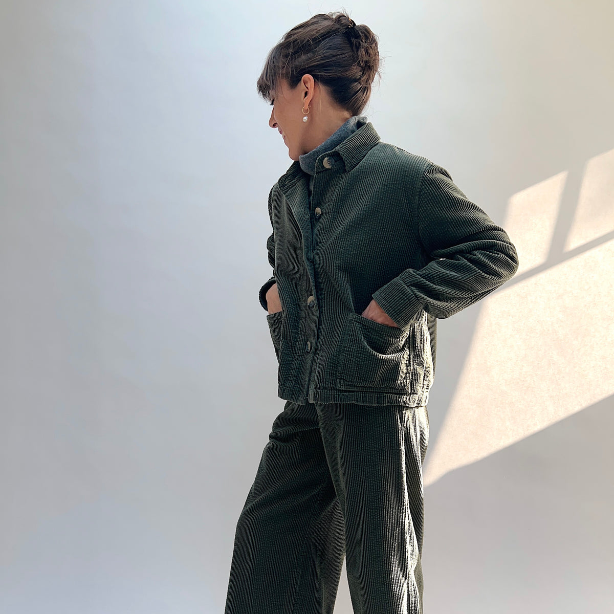 Angled view of the Lux Corduroy Cropped Jacket in Kelp, with the model’s hands in the front patch pockets.
