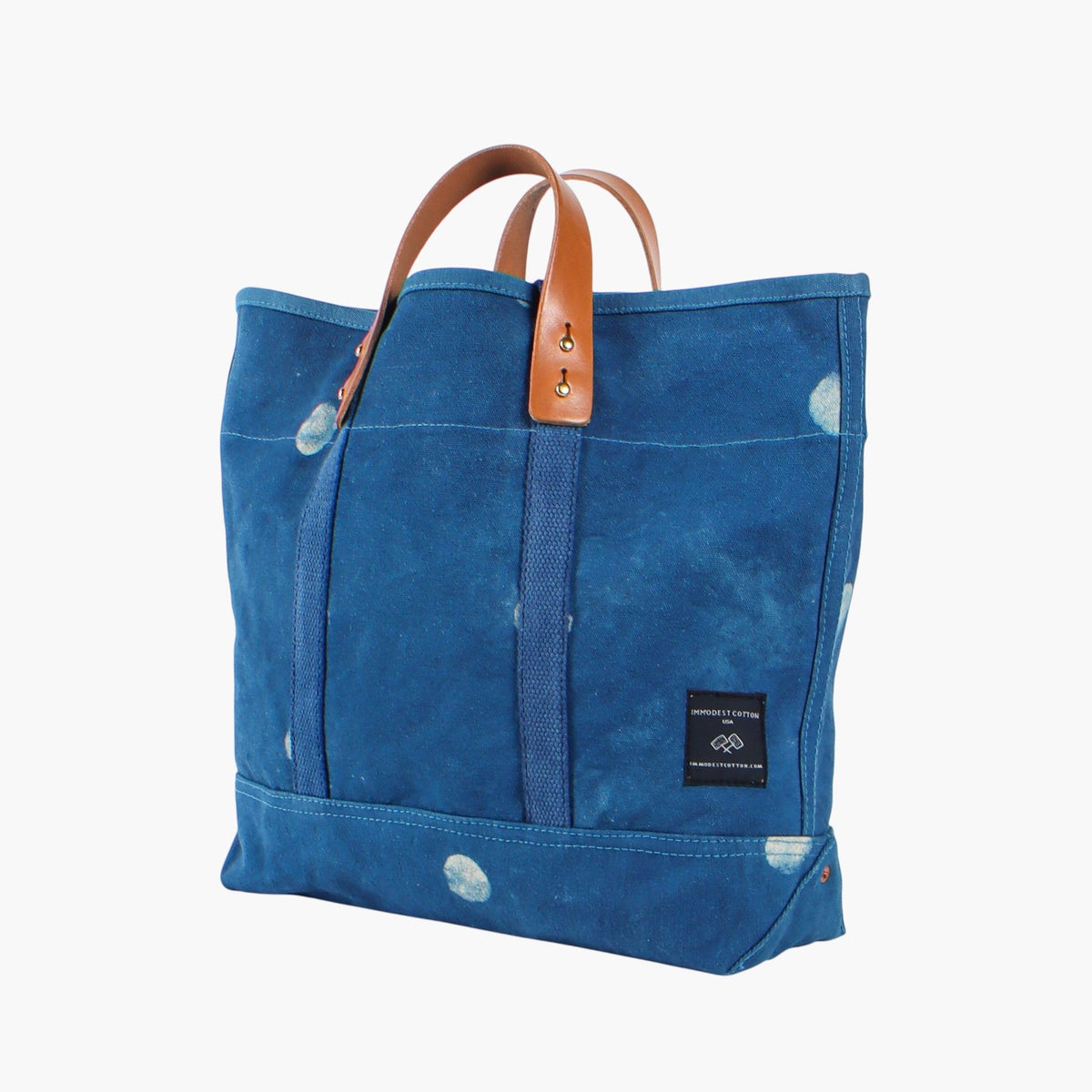 Angled view of the Small Light Indigo Moon tote showing its side seam, base, leather handles, and brand label.
