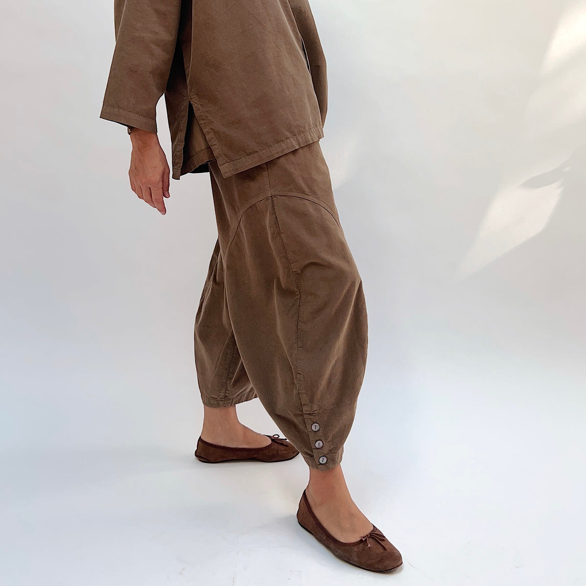 Eleven Stitch Corduroy Doreen Pant in Winter Olive, side view showing the balloon leg silhouette tapering to a gathered ankle cuff with three shell buttons, styled with a matching corduroy top and brown ballet flats
