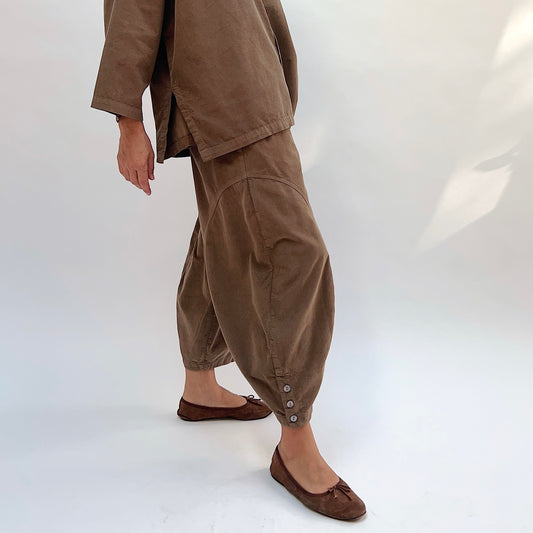 Eleven Stitch Corduroy Doreen Pant in Winter Olive, side view showing the balloon leg silhouette tapering to a gathered ankle cuff with three shell buttons, styled with a matching corduroy top and brown ballet flats
