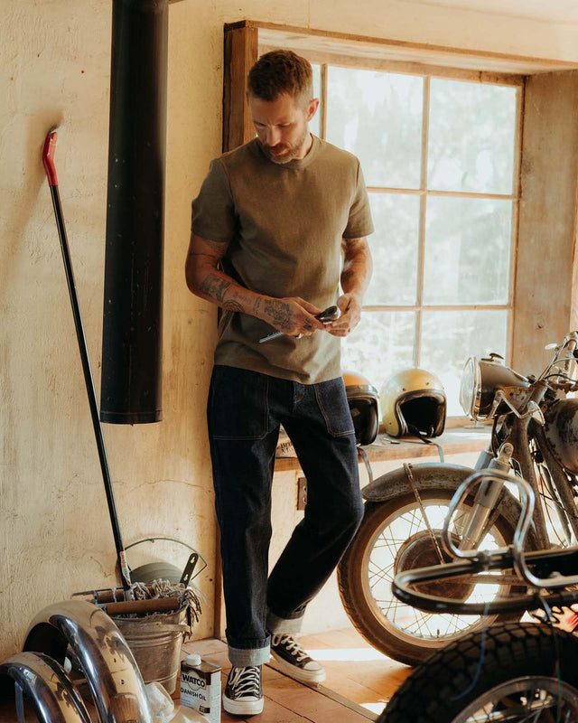Close-up of man wearing the Taylor Stitch Organic Cotton Shop Tee in Army Twist, showing ribbed crewneck, shoulder seam detail, and cuffed sleeve on heathered army green cotton jersey
