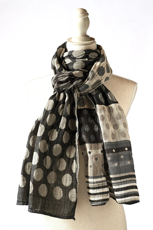 Létol Coline Scarf in Noir Gris, draped and knotted on a linen dress form against a white background, showing a reversible Jacquard-woven organic cotton scarf — one side featuring large oatmeal and beige polka dots on a deep black ground, the other showing a light chambray and beige ground with smaller dots and a bold black and grey striped border — with the fringe edge visible at the hem

