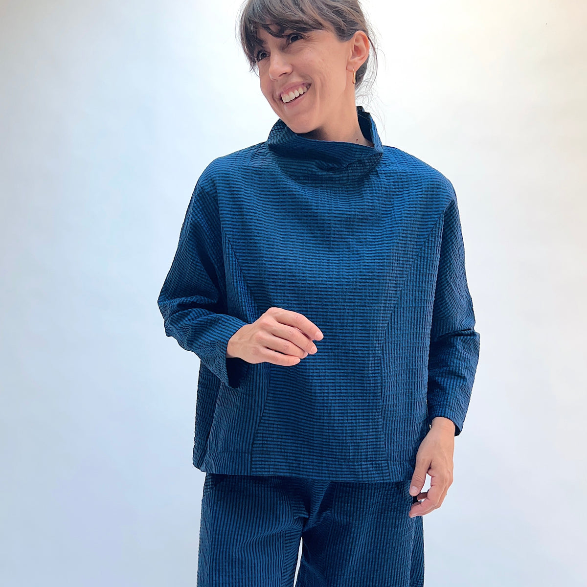 Niche Sofi Top in Blue Seersucker Stripe, front view showing the high funnel neck and relaxed boxy fit in teal and black seersucker stripe
