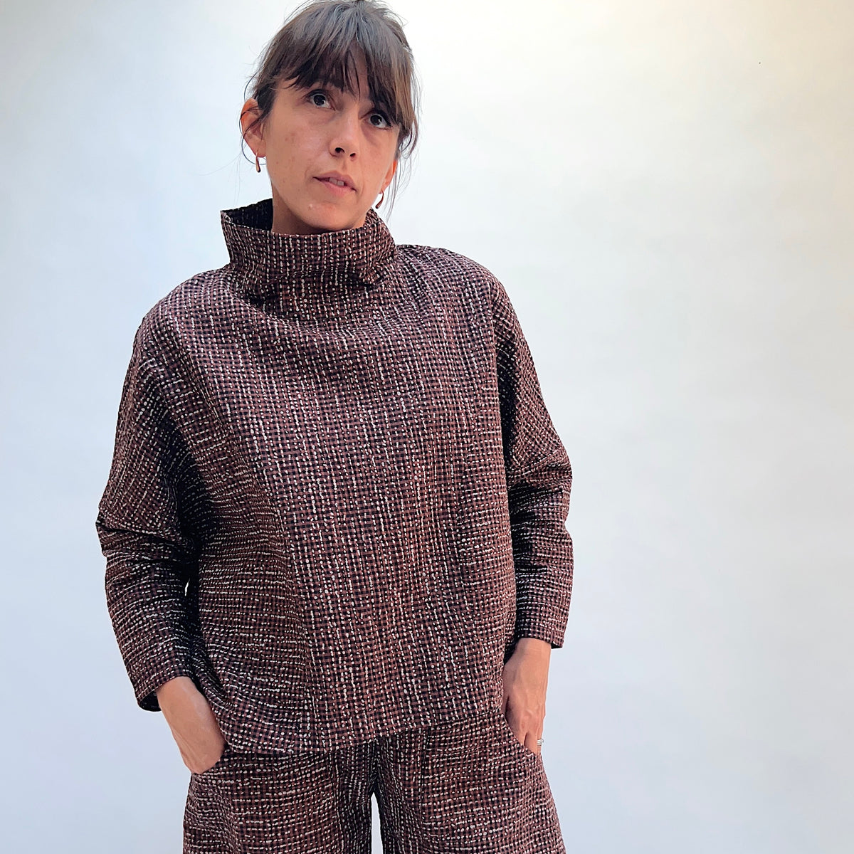 Niche Sofi Top in Cocoa Check, front view showing the high funnel neck and relaxed boxy fit in dark brown textured check with contrast black cuffs
