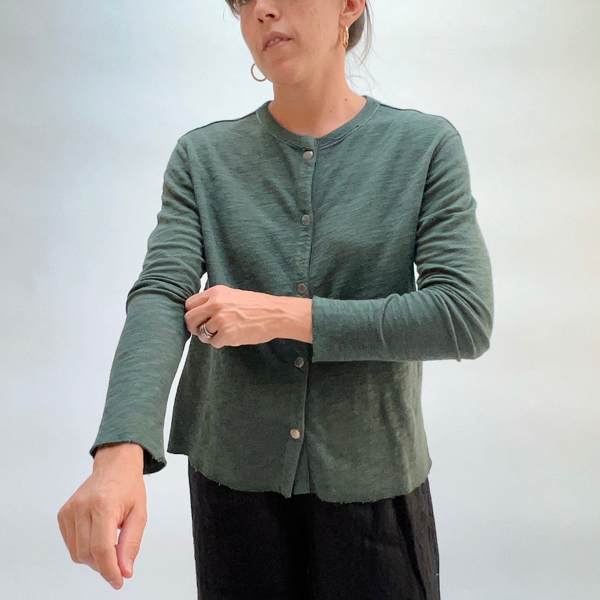 Model wearing the Cut Loose Snap Front Cardigan in Konbu, back view, showing relaxed silhouette and raw curved hem in deep teal green cotton
