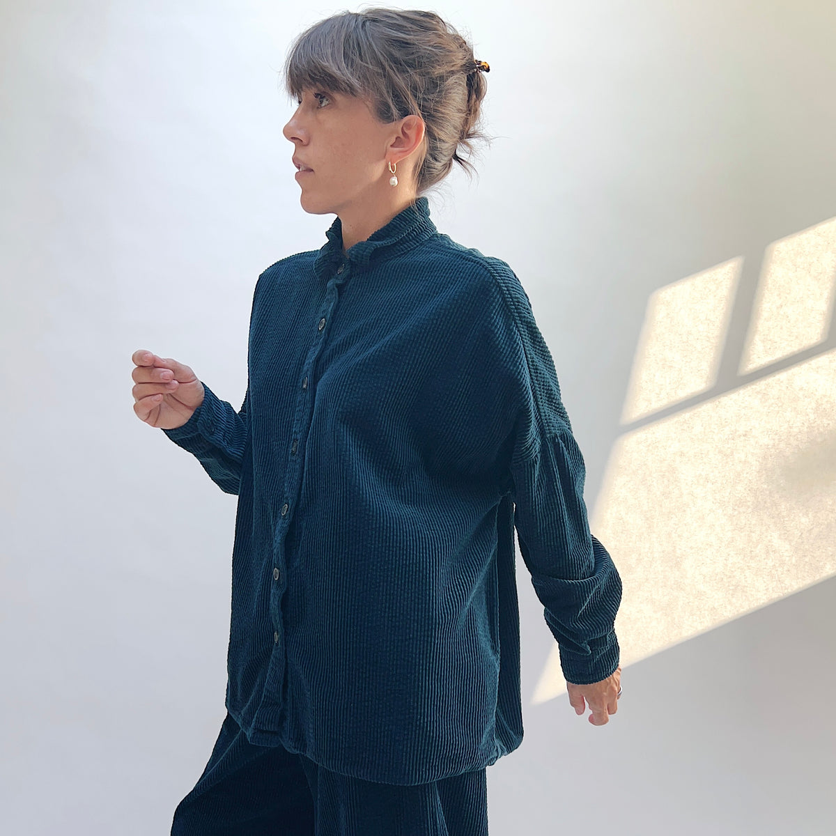 Side view of the Lux Corduroy Oversized Shirt in Etan on a model, showing the dropped shoulders, long sleeves, and curved hem.
