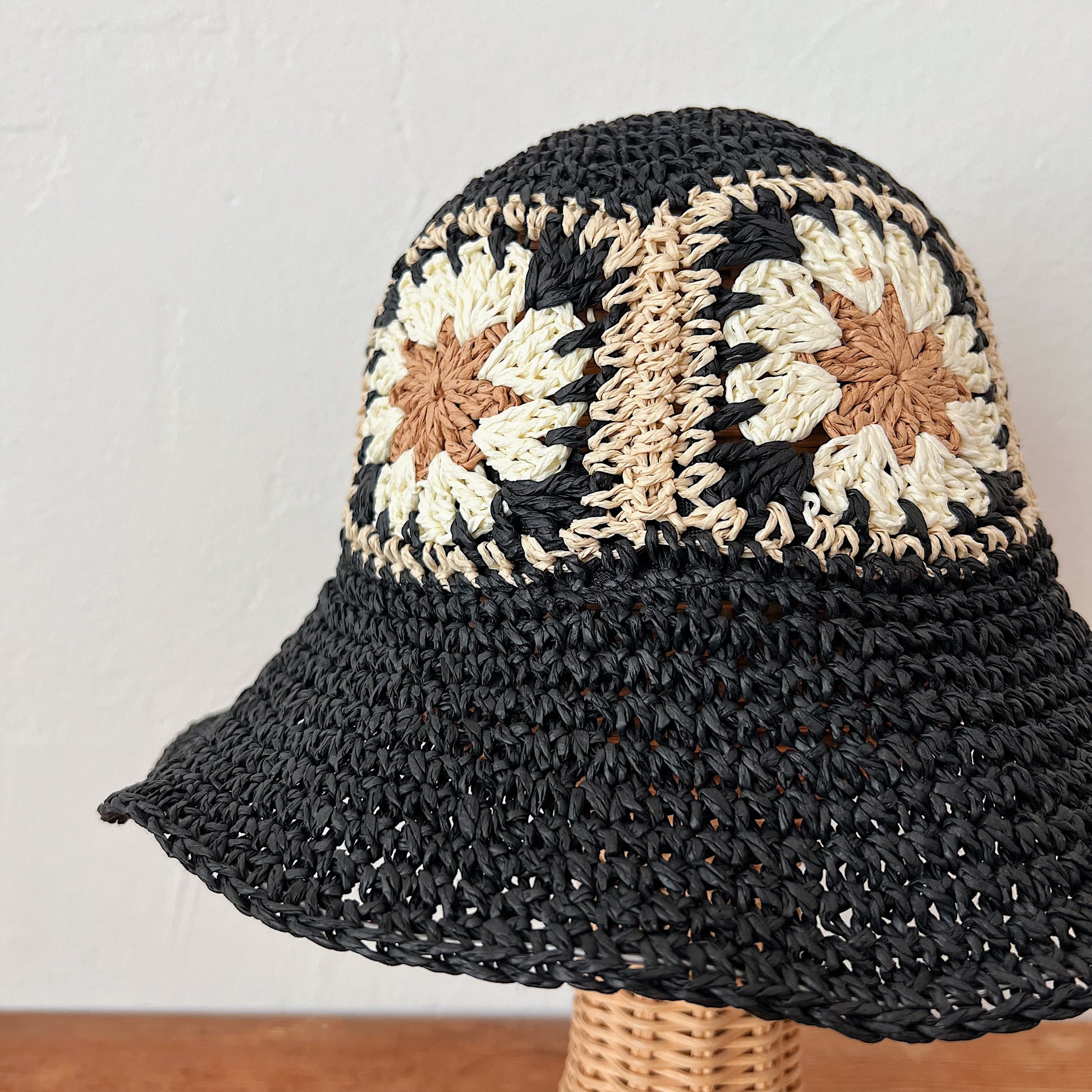 Close-up of black paper crochet bucket hat showing open-weave brim and cream and tan floral granny square crown detail