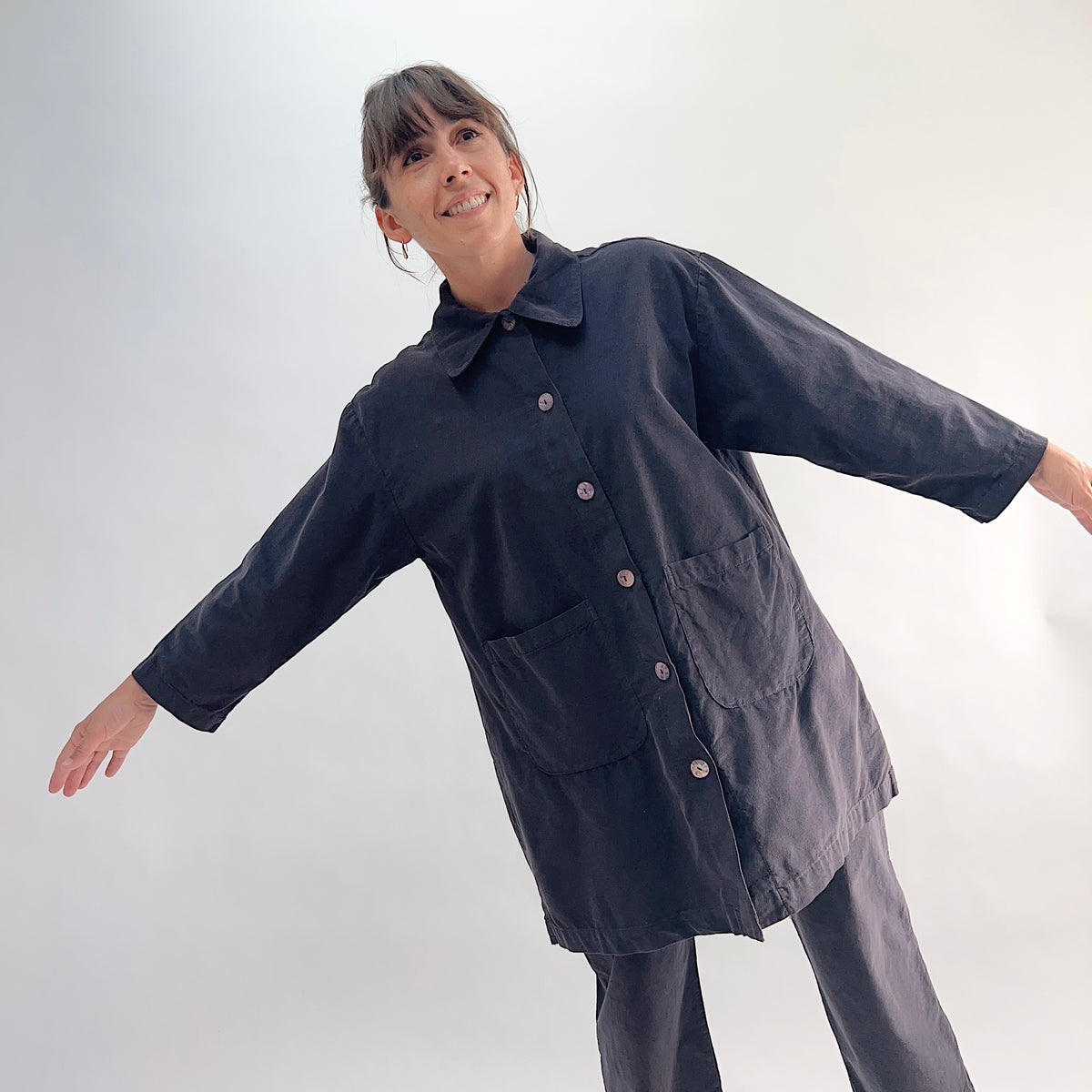 Model with arms outstretched wearing the Bryn Walker Corduroy Car Coat in Fig, front view showing rounded point collar, mother of pearl buttons, two large front patch pockets, 3/4 sleeves, and deep fig pinwheel corduroy, styled with matching corduroy pants
