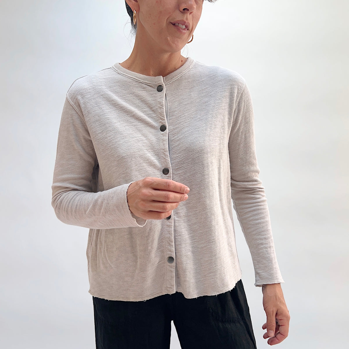 Model wearing the Cut Loose Snap Front Cardigan in Nimbus, front view, fitted snap-front cotton cardigan in light heathered gray with raw hem, styled with black trousers
